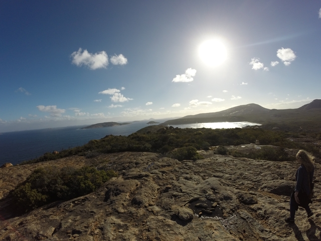       Person sitting on a rock overlooking the sea with a bright sun.
  