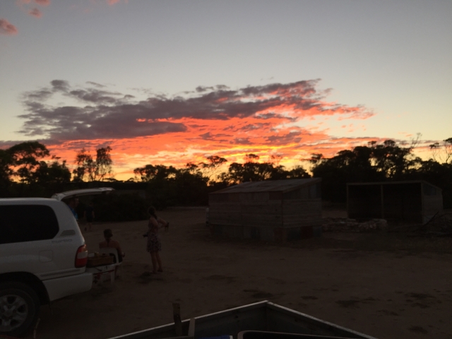       Silhouette of people and a vehicle at sunset in a rural setting.
  
