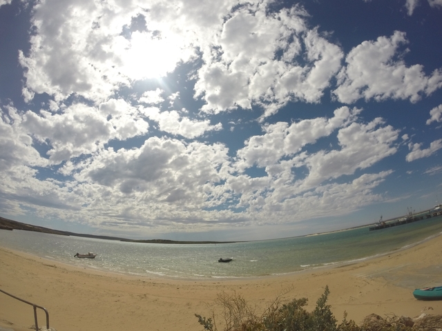       Sandy beach with calm water and boats under a cloudy sky.
  