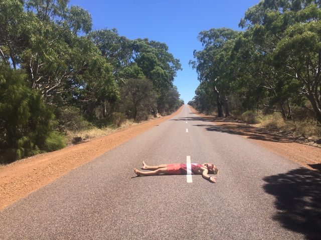       Person lying on a rural road surrounded by trees.
  
