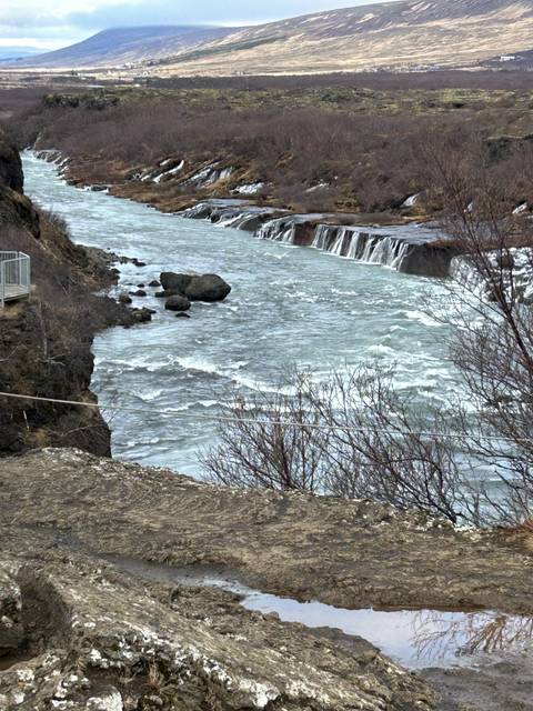       Icy river with small waterfalls in a rugged landscape.
  