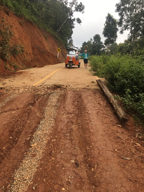 Person walking uphill on a dirt road with a tuk-tuk.