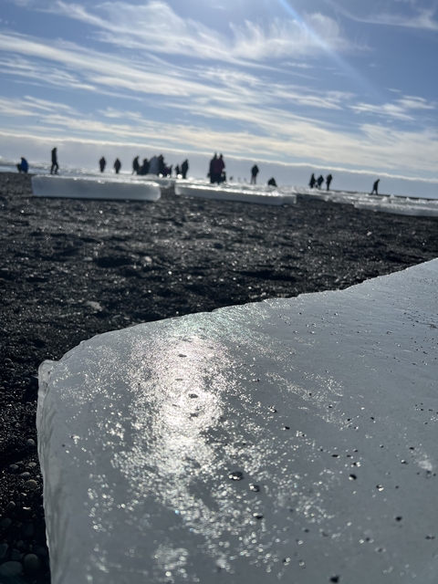       Ice on black sand beach with people in the background.
  
