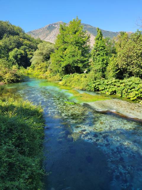       Clear blue stream surrounded by lush greenery and hills.
  