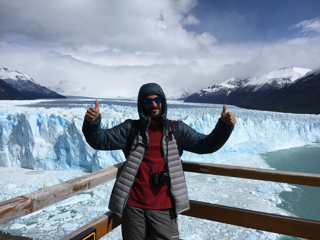       Person posing with thumbs up in front of a large glacier.
  