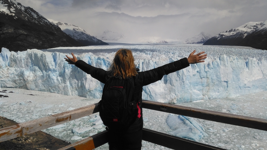       Person with arms spread wide in front of a massive glacier.
  