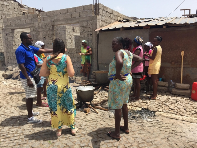       People cooking and talking on a cobblestone street.
  