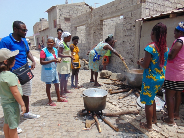       People preparing food over open fires on a street.
  