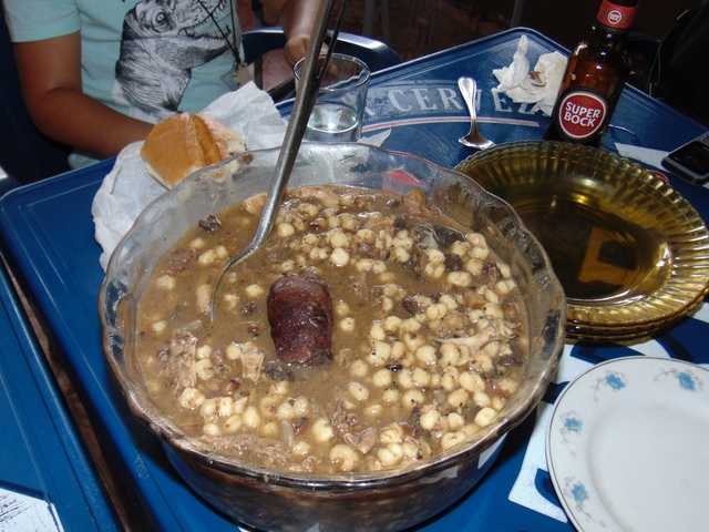       Bowl of traditional dish on a table with a glass of beer.
  