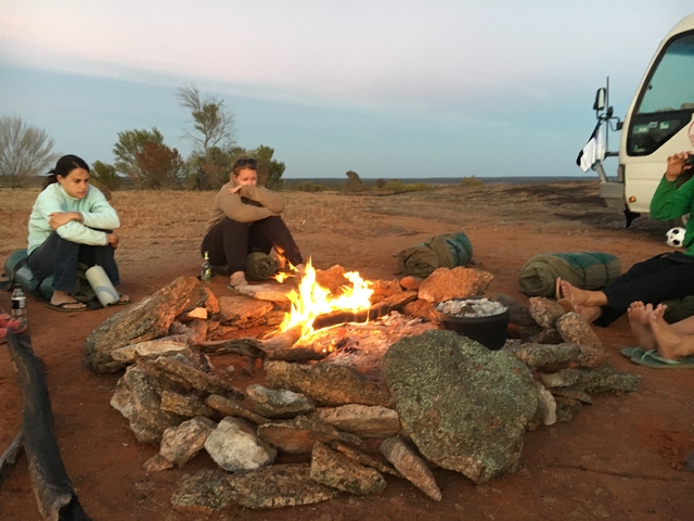Group of people sitting around a campfire in a rugged landscape.