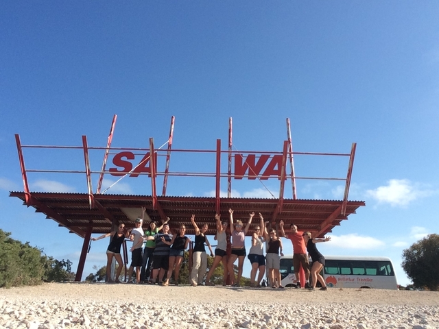 Group of people posing on a structure with a sign in the background.