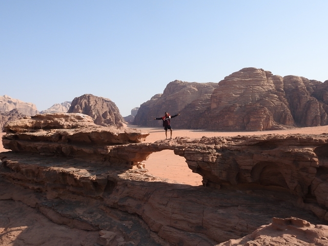       Person standing on a large rock formation in a desert landscape.
  