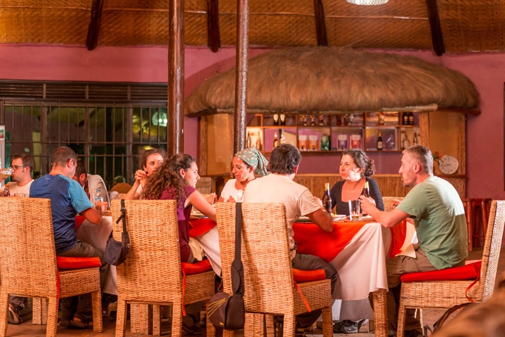       A group enjoying dinner in a traditional setting with a thatched roof.
  