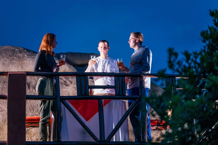       Three people on a deck enjoying drinks with thatched roofs in the background.
  