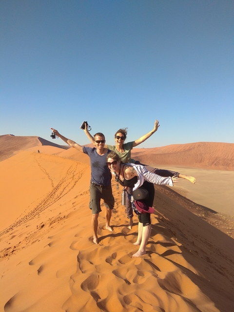 Friends posing on a sand dune with energetic expressions.