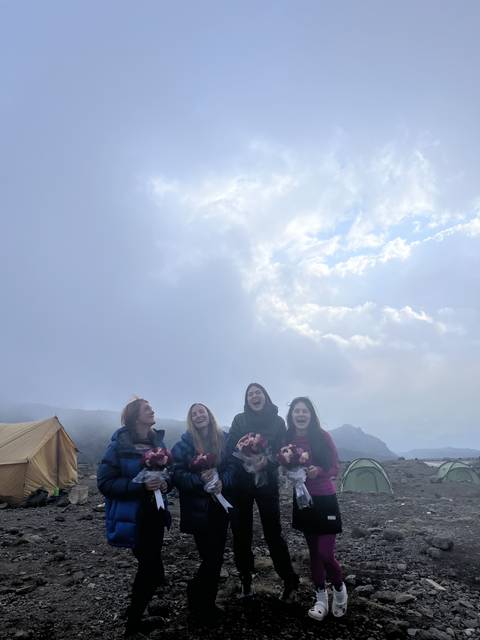 Group of women smiling with flowers on a mountain.