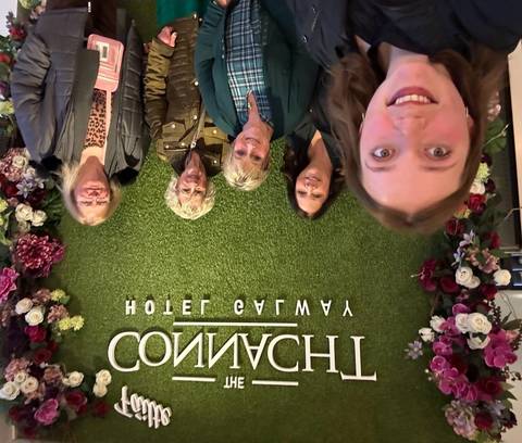 Group of people posing in front of a floral wall with text.