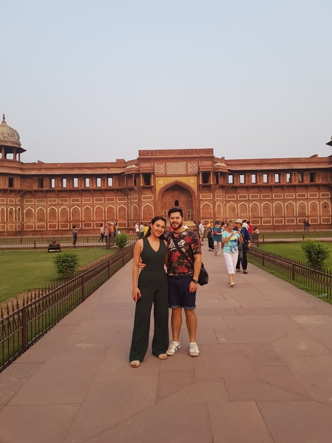 Couple posing in front of a historic red fort with a crowd in background.