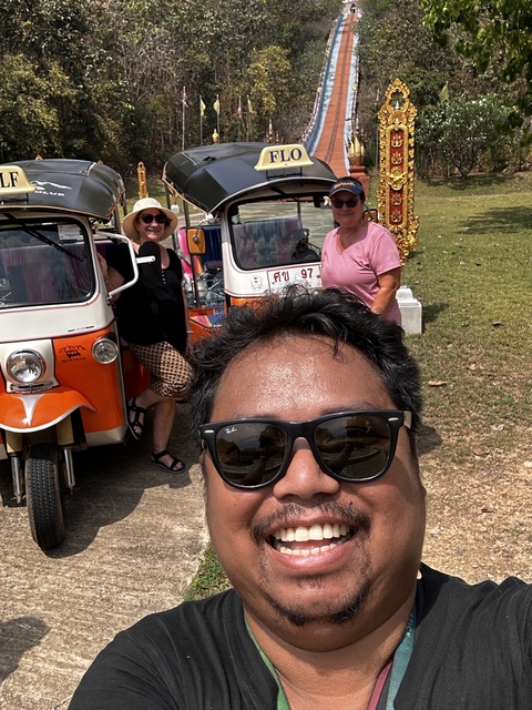 Group of people posing with tuk-tuks in the background.