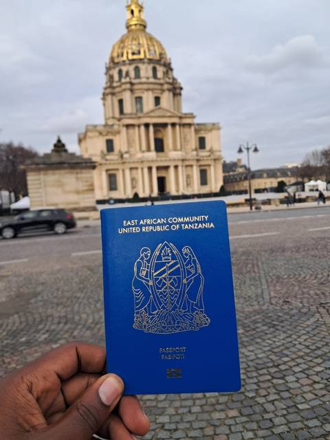 Person holding a Tanzanian passport with a historic building in the background.