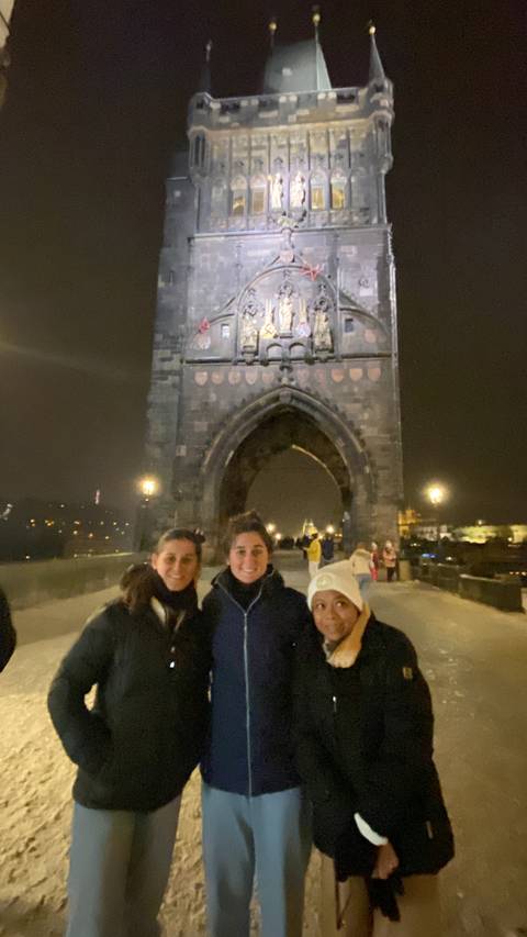 Three people posing at night in front of a Gothic-style tower.