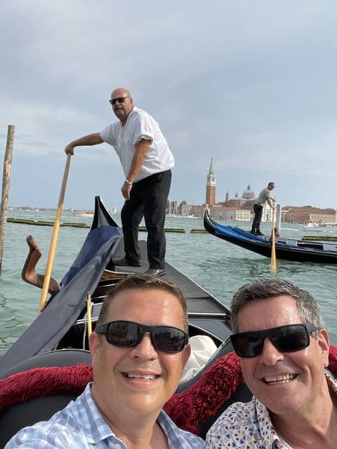 Gondolier rowing a gondola with two passengers in a canal.