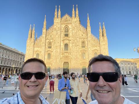Two men posing with the Milan Cathedral's facade visible.