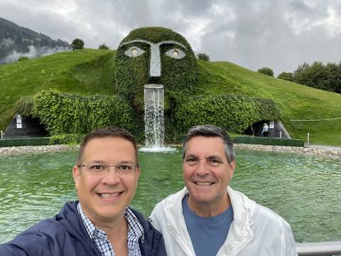Men posing in front of a water feature surrounded by greenery.