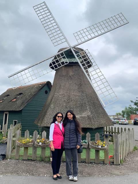 Two women standing in front of a traditional windmill.