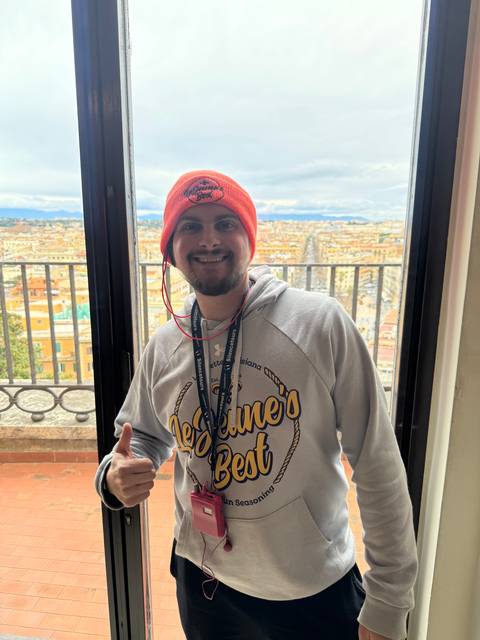 Person posing indoors with a landscape painting in the background.