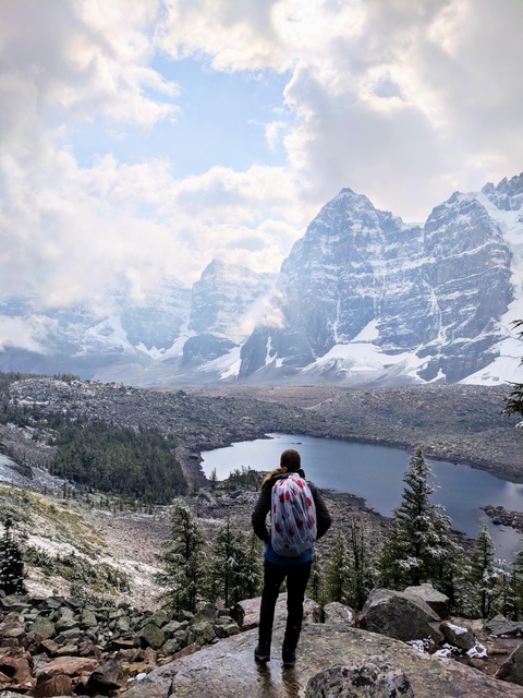 Person with a backpack overlooking a mountain with a lake.