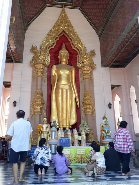 Tall golden Buddha statues in a temple with visitors.