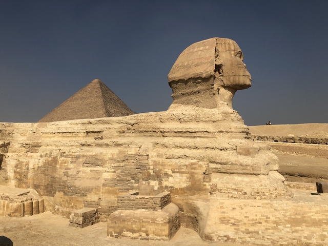 The Sphinx with a backdrop of a pyramid in the desert.
