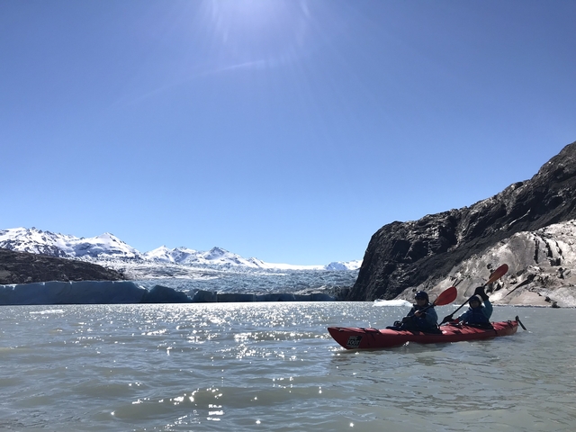       Two people kayaking on a glacier lake.
  