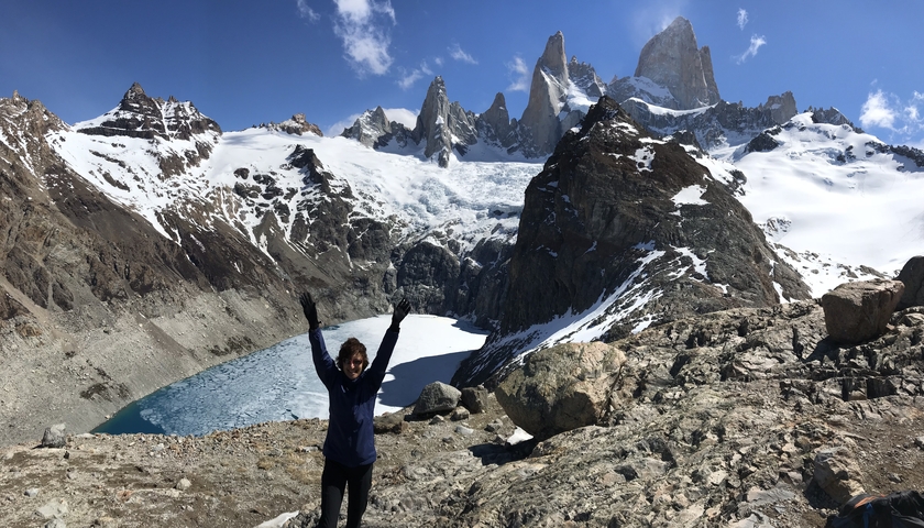       Person with arms raised in front of snow-capped mountains.
  