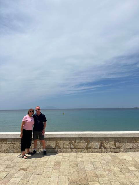       Two people posing in front of a seaside promenade.
  