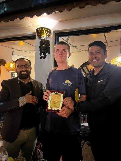 Three individuals celebrating indoors, one holds a plaque.