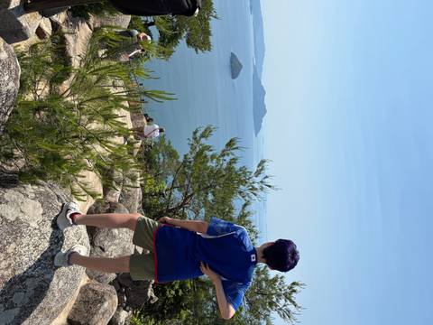      Person standing on a rocky hill with ocean view.
  