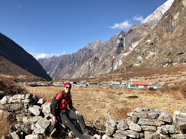       A person sitting on a stone wall with a mountainous village in the background.
  