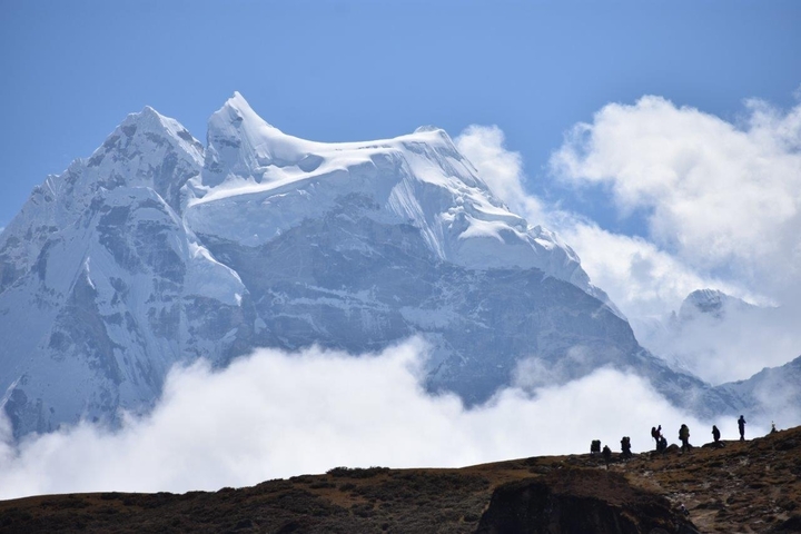 Silhouettes of hikers against a backdrop of a snow-capped mountain.