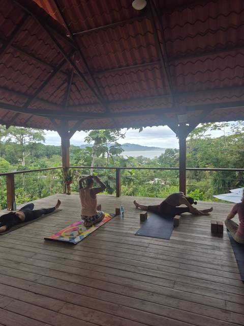 People practicing yoga on a wooden deck overlooking lush greenery.