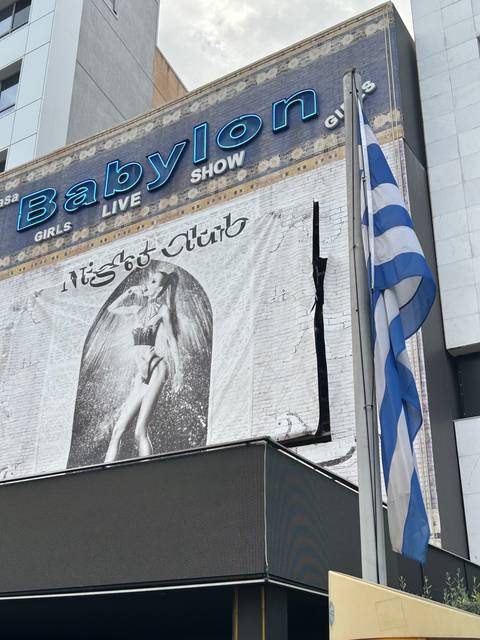 Signage of a building with partially obscured text and a Greek flag.