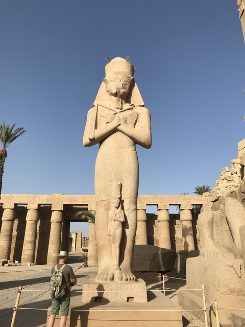 Ancient Egyptian statue standing tall against a blue sky.