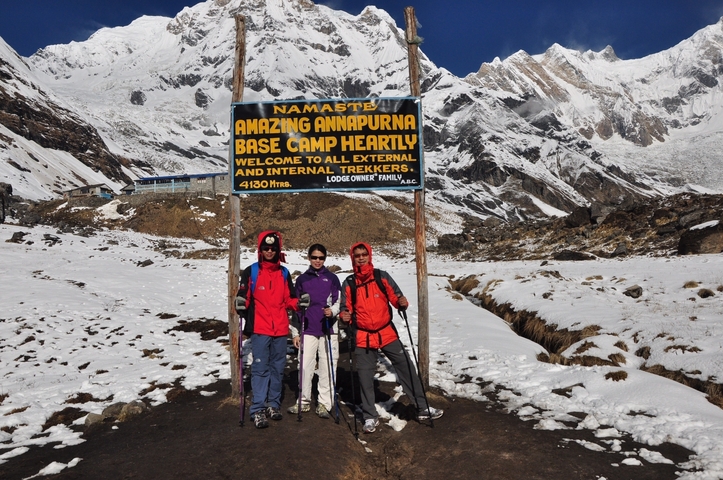       Hikers posing at the Annapurna Base Camp with snowy mountains.
  