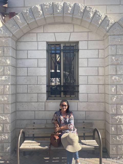 Woman sitting on a bench against a white stone wall with a window.