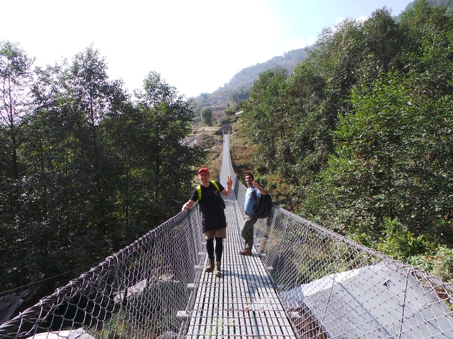       People crossing a long suspension bridge in a forested area.
  