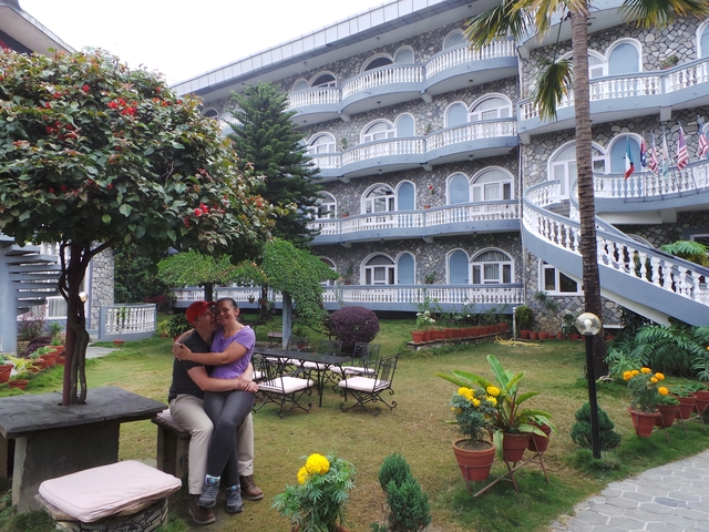       Couple embracing in a courtyard with a distinctive building behind.
  