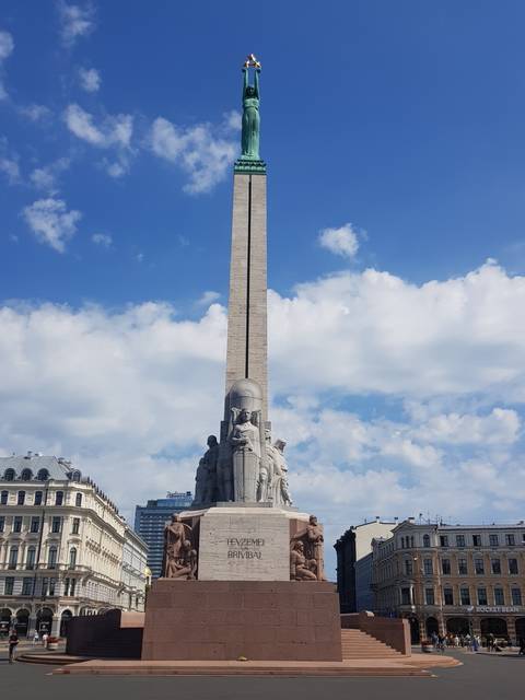       A tall monument with statues on a stone base under a blue sky.
  