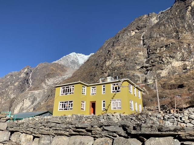 A yellow house with mountains in the background in a rural setting.