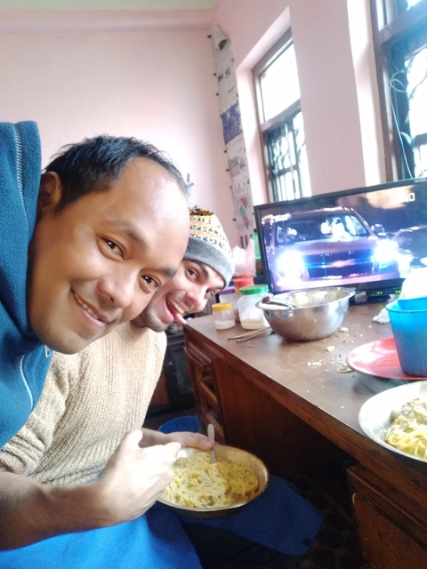 Two people smiling with a television in the background showing action scenes.